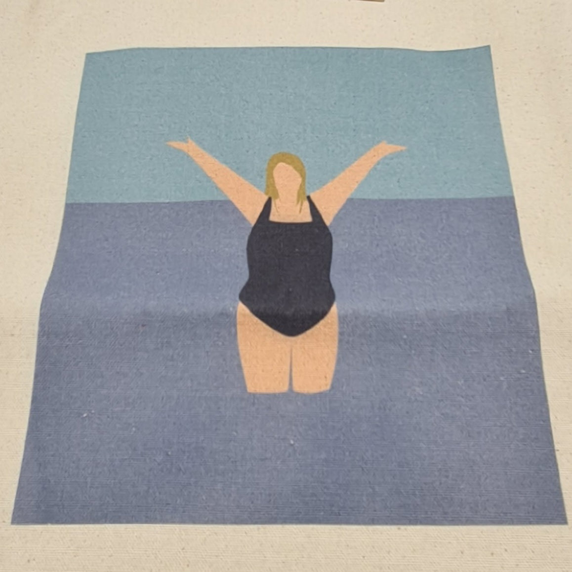 Close up of image on the "I Love the Water" tote bag. It features an illustration of a woman standing in the sea wearing a dark swimsuit. She is holding her arms up in joy. 