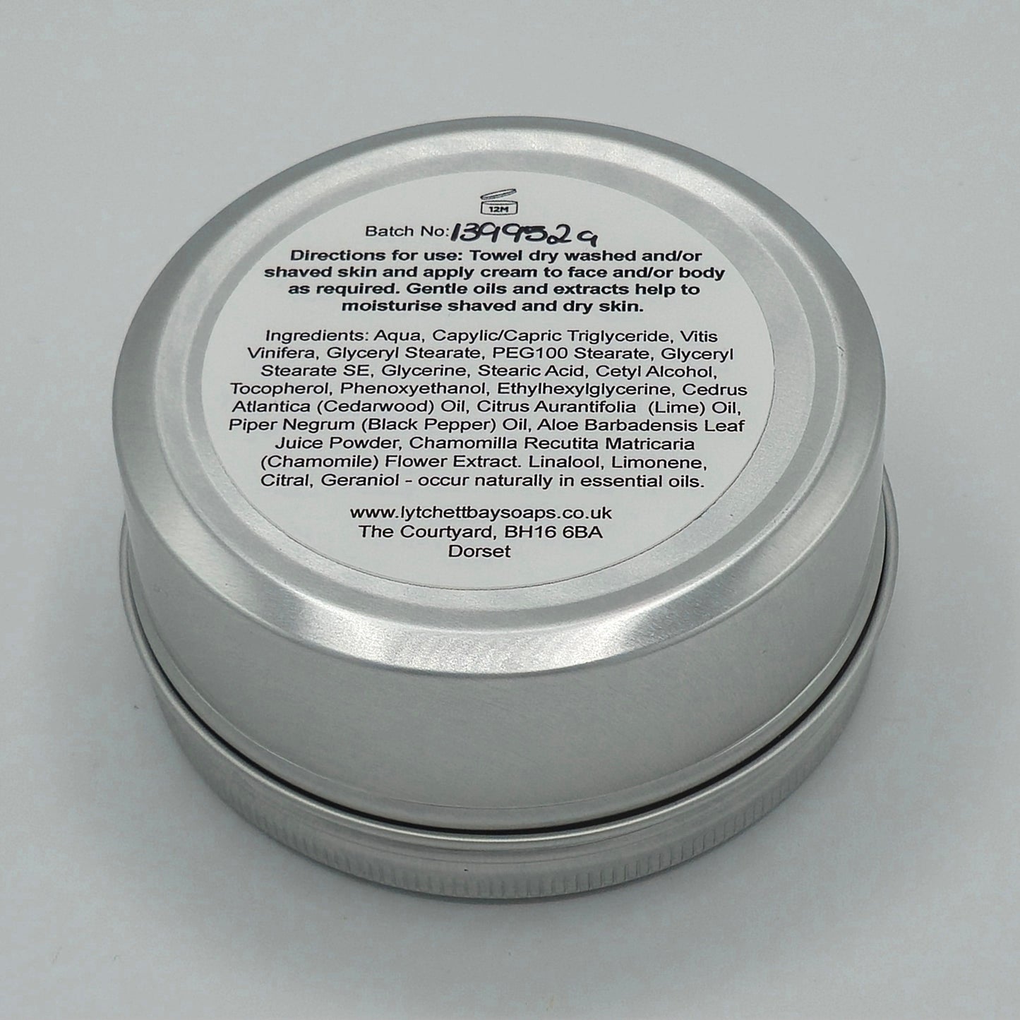 The back or bottom side of the silver tin containing Aftershave, Face & Body Cream for Men by Lytchett Bay Soaps. At the top of the label is that batch no, then bold text saying "Directions for use: Towel dry washed and/or shaved skin and apply cream to face and/or body as required. Gentle oils and extracts help to moisturise shaved and dry skin".
Half down the label there is text containing the ingredients. 