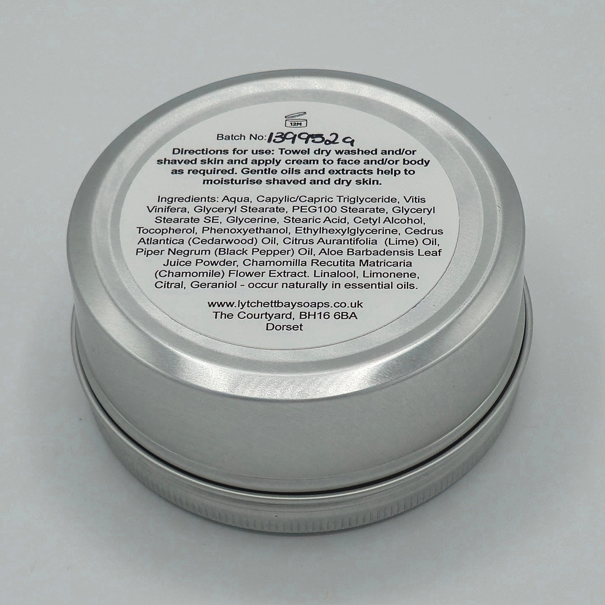 The back or bottom side of the silver tin containing Aftershave, Face & Body Cream for Men by Lytchett Bay Soaps. At the top of the label is that batch no, then bold text saying "Directions for use: Towel dry washed and/or shaved skin and apply cream to face and/or body as required. Gentle oils and extracts help to moisturise shaved and dry skin".
Half down the label there is text containing the ingredients. 