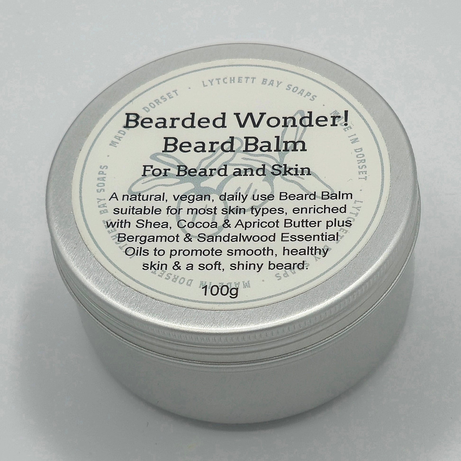 Round silver tin, around 7cm diameter, with light coloured label saying "Bearded Wonder! Beard Balm For Beard and Skin. A natural, vegan, daily use Beard Balm suitable for most skin-types, enriched with Shea, Cocoa & Apricot Butter plus Bergamot & Sandalwood Essential Oils to promote smooth, healthy skin & a soft, shiny beard. 100g".