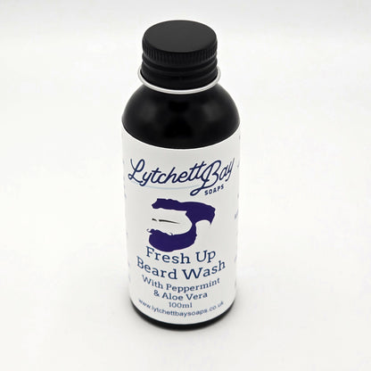 Small black glass bottle with a black lid and white label saying "Lytchett Bay Soaps", featuring an illustration of a man with a beard and the text "Fresh Up Beard Wash with Peppermint & Aloe Vera, 100ml".