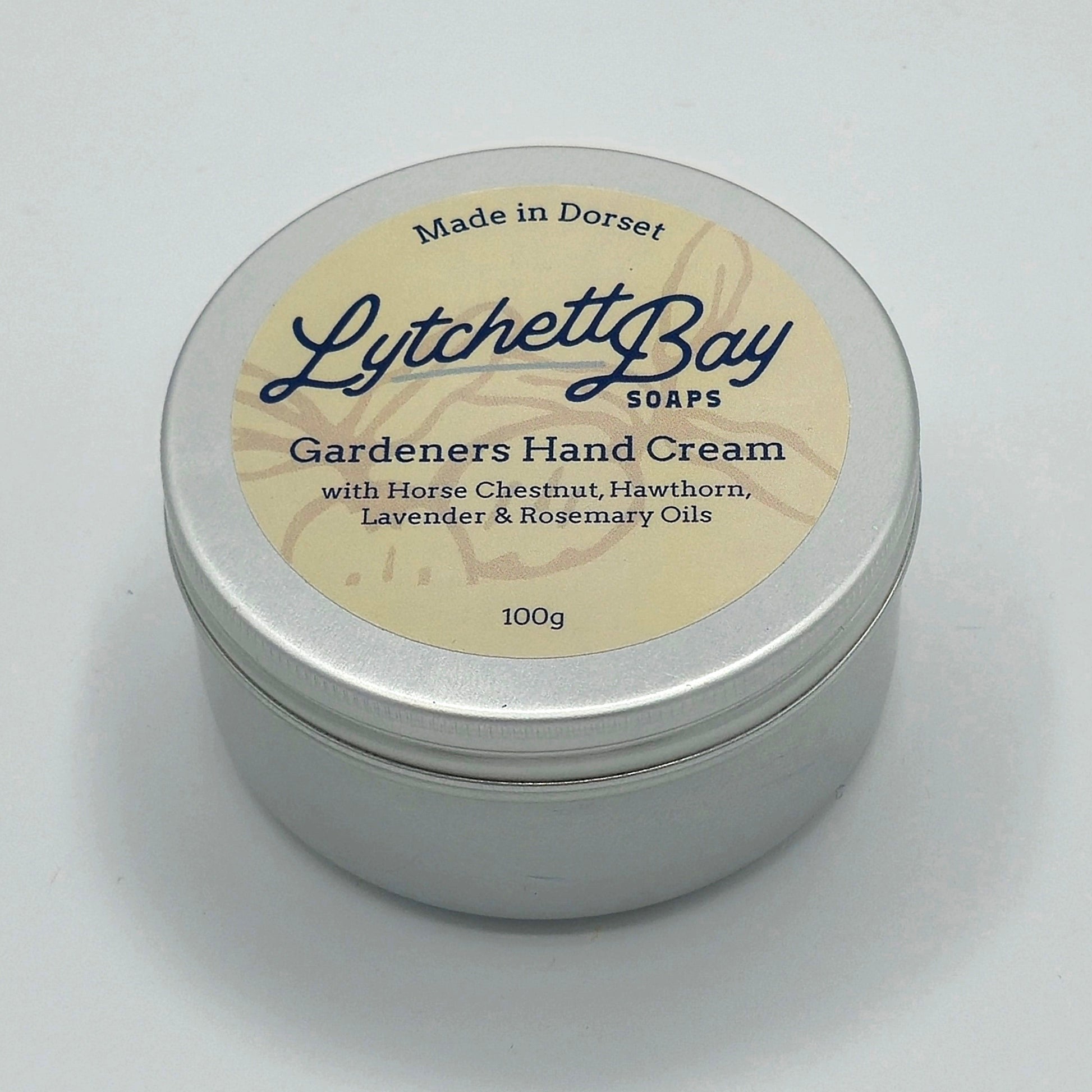 Small round silver tin with a cream coloured label saying "Lytchett Bay Soaps Gardeners Hand Cream with Horse Chestnut, Hawthorn, Lavender & Rosemary Oils. 100g".