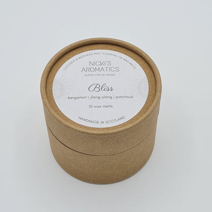 Round kraft cardboard box with a white label on the top with the text "Coconut & Rapeseed Wax Essential Oil Wax Melts" along the top. Below this is the logo for "Nicki's Aromatics" and the strapline "Scents for the Senses". In the middle of the label is the name "Bliss" with "Bergamot", "Ylang-Ylang" "Patchouli" and "10 wax melts" typed below. At the very bottom of the label is the wording "Handmade in Scotland".