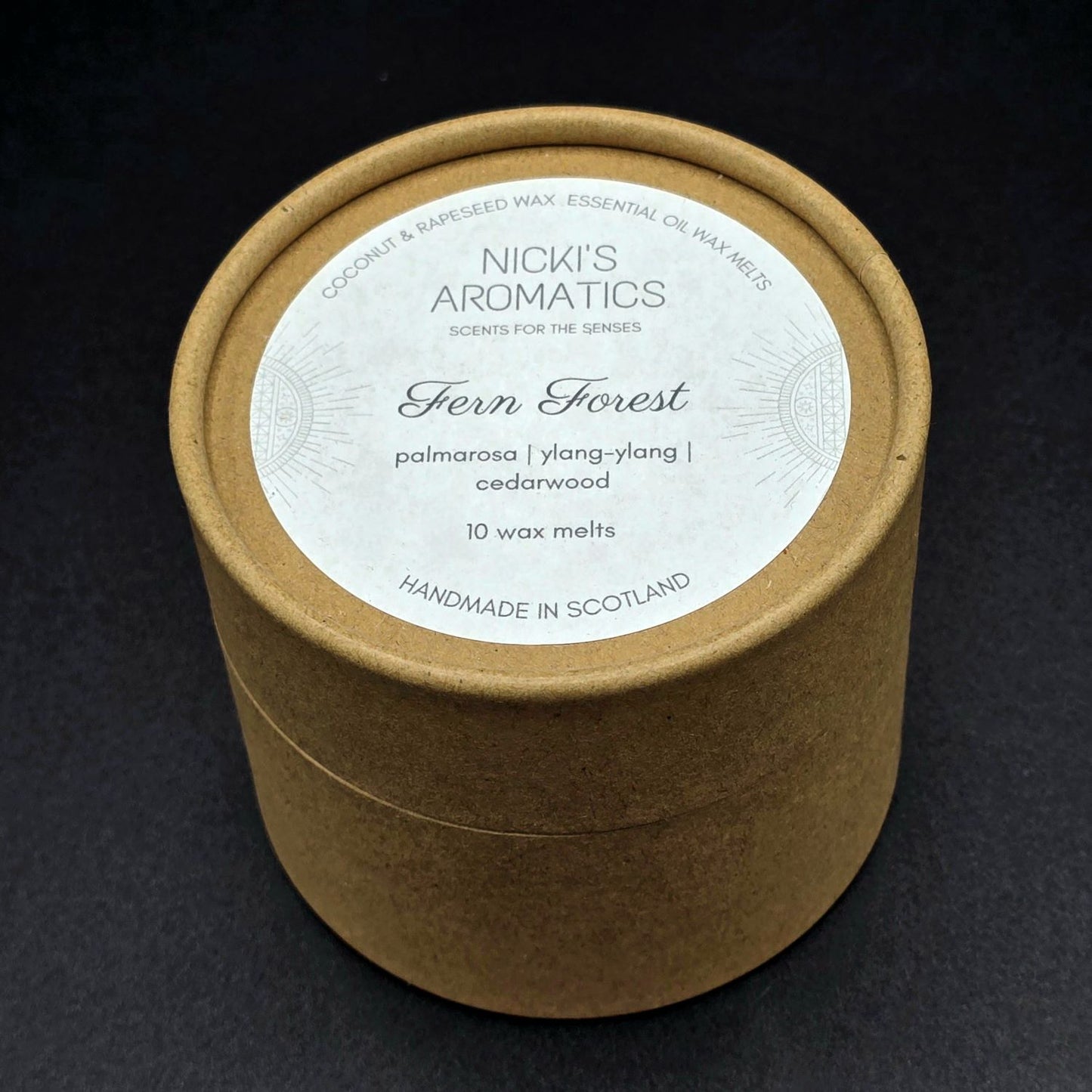 Brown kraft round cardboard box containing 10 wax melts. The label says "Fern Forest - Palmarosa, Ylang-Ylang, Cedarwood".