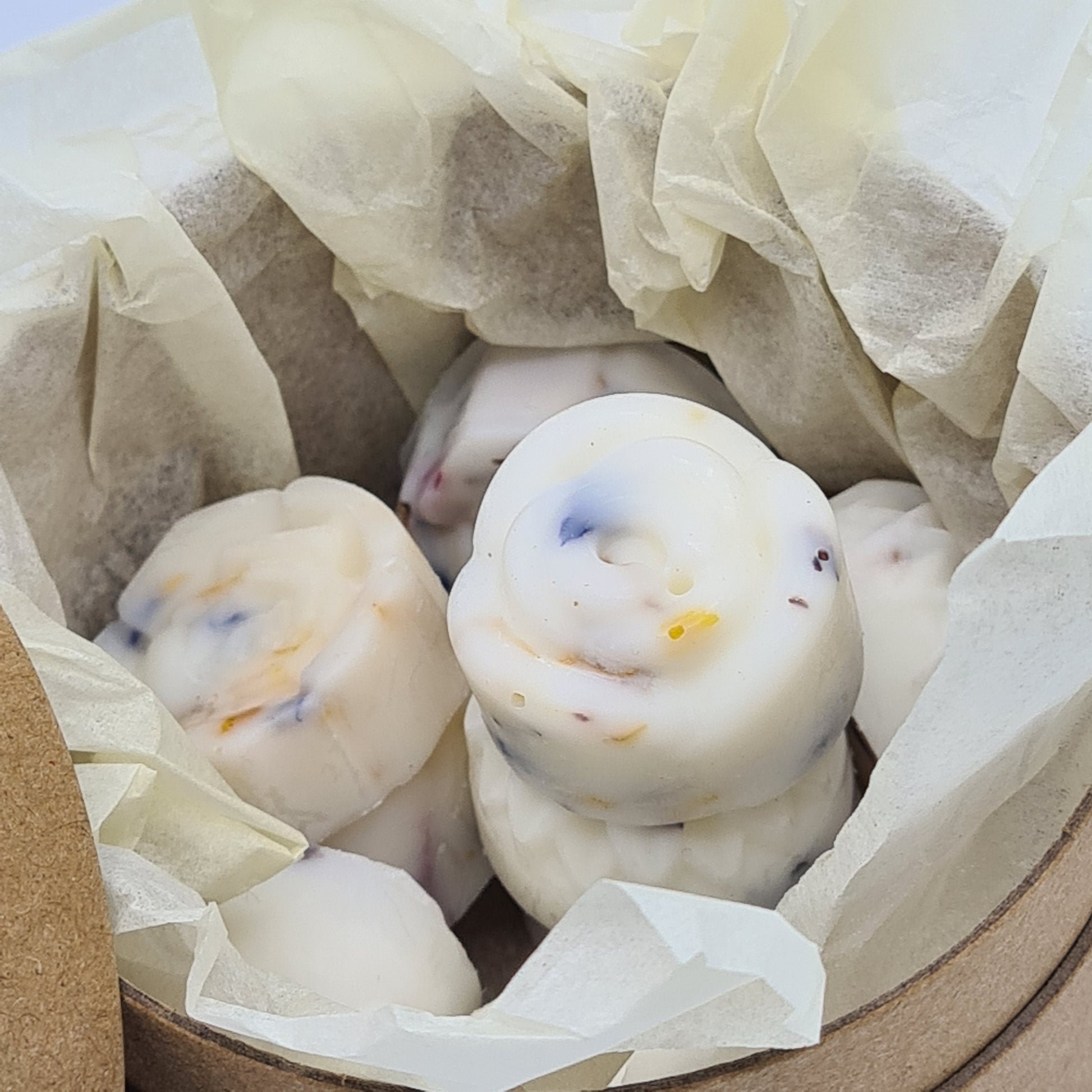 Close up image of the inside of the round cardboard tube containing wax melts. It shows flower shaped wax melts, infused with flower petals. These are encased inside ivory tissue paper.