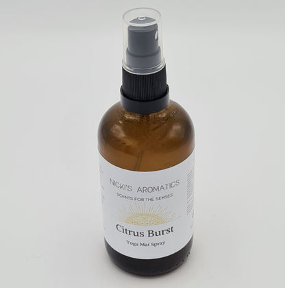 Amber glass spray bottle with clear plastic lid. At the top of the white label is the logo for "Nicki's Aromatics" with the strapline "Scents for the Senses" and at the bottom of the label is the text "Citrus Burst Yoga Mat Spray".