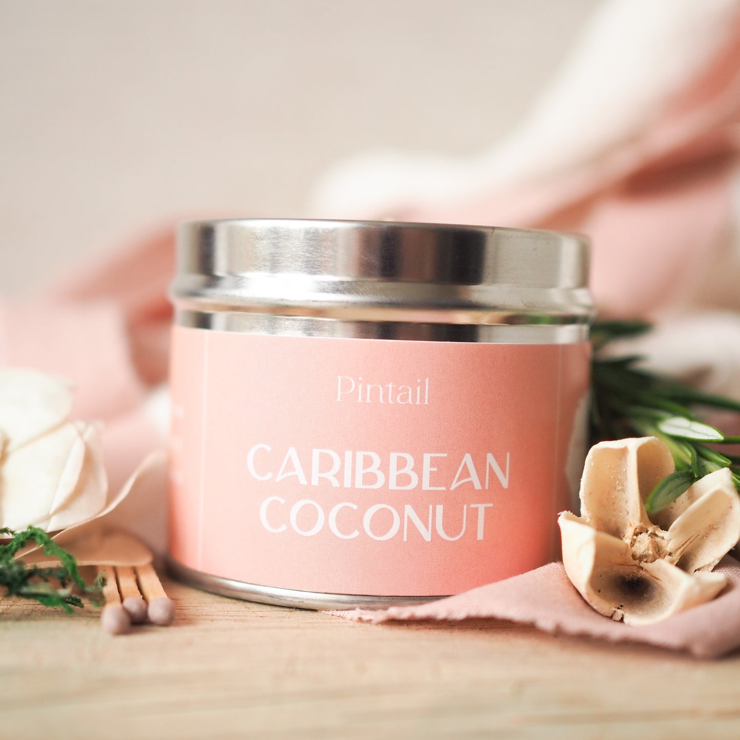 Classic tin candle from Pintail with a pink label with white writing. The label has "Pintail" at the top and the fragrance "Caribbean Coconut" written below.