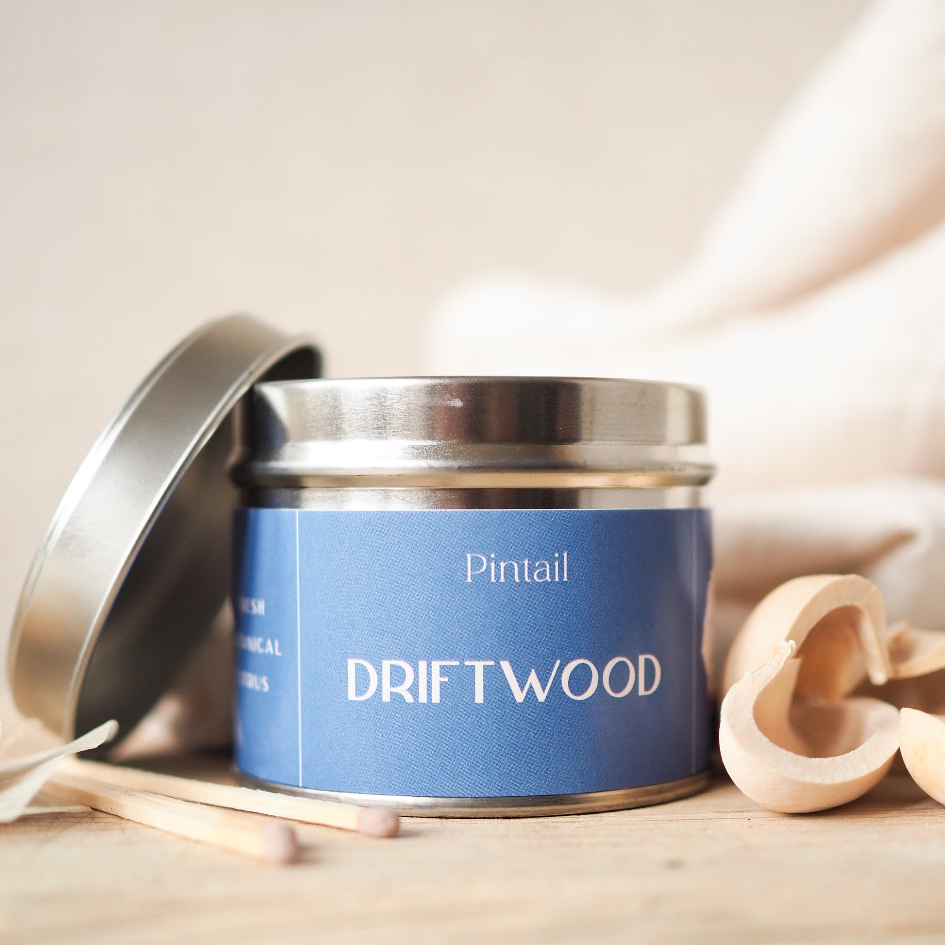 Petite paint pot candle from Pintail Candles. It has a blue label with white writing. The label has "Pintail" at the top with the fragrance "Driftwood" written below.