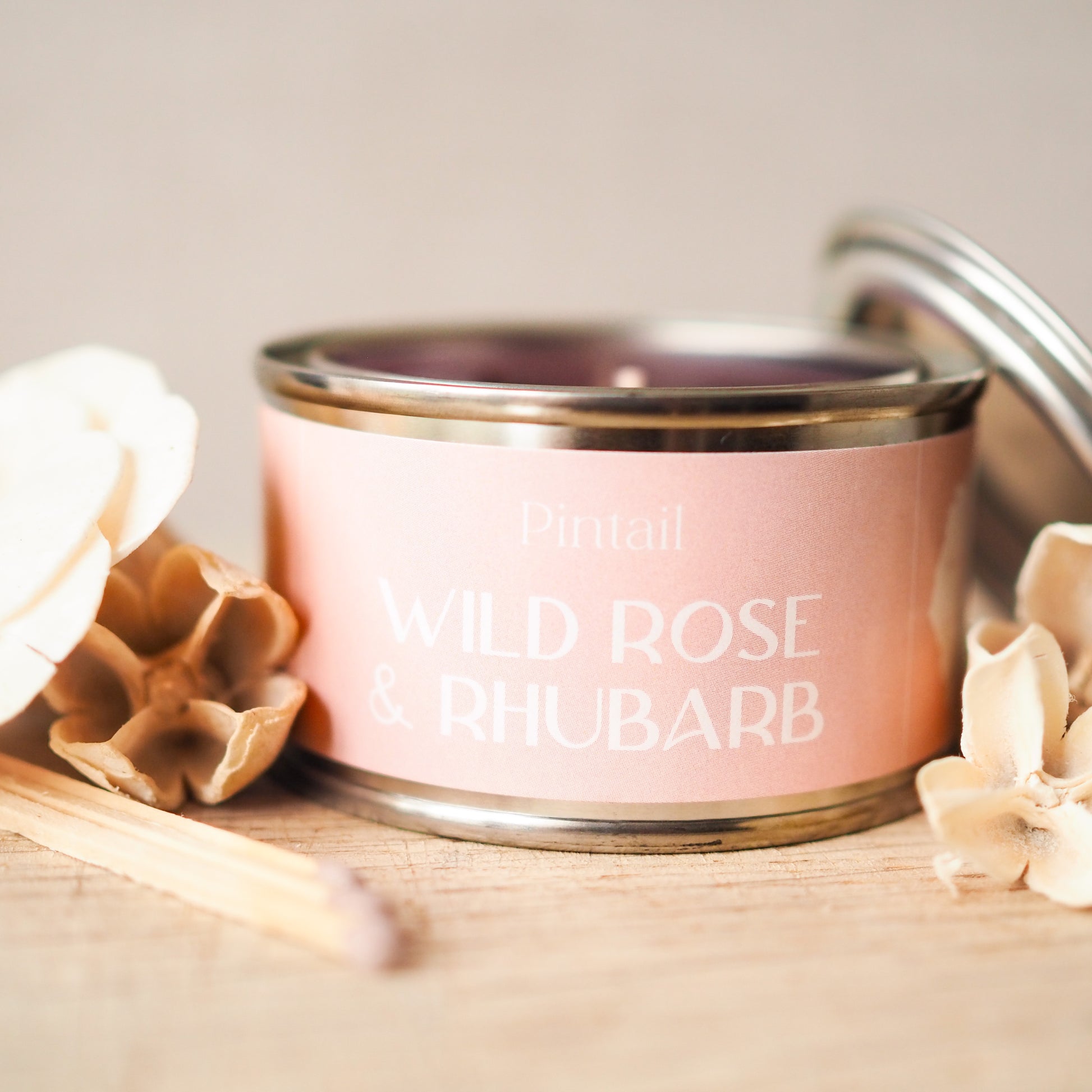 Small tin candle from Pintail with a pink label. The label has the name Pintail at the top and the fragrance "Wild Rose & Rhubarb" written below. 