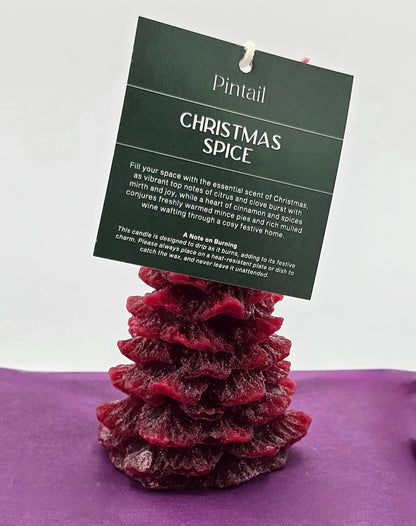 Red candle shaped like a Christmas tree with a 'Pintail' Christmas Spice label on a purple surface.