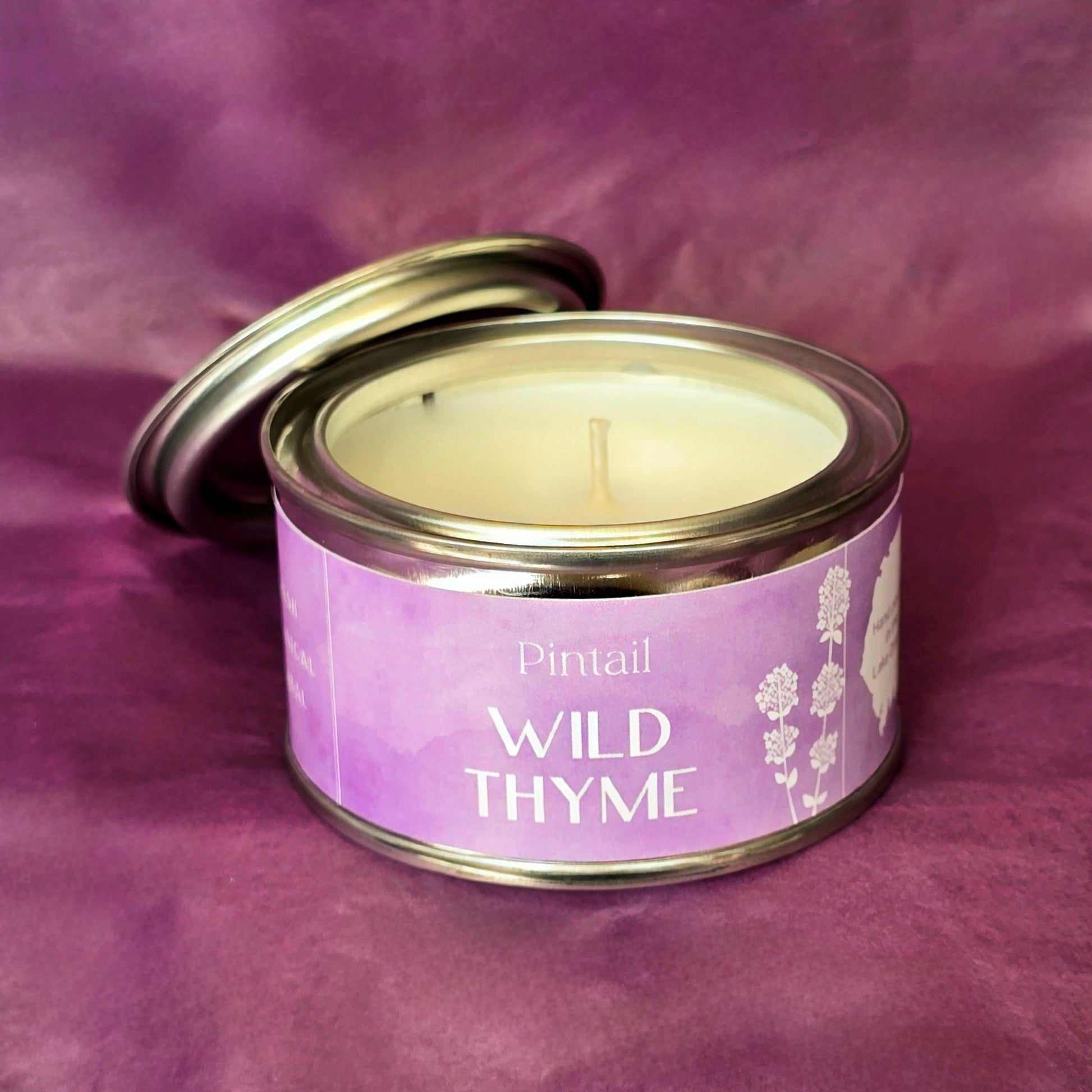 Petite paint pot candle tin from Pintail Candles. The lilac coloured label on the tin says "Wild Thyme" and features an illustration of white flowers. The tin is open showing the white candle and wick inside. 