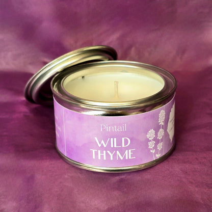 Petite paint pot candle tin from Pintail Candles. The lilac coloured label on the tin says "Wild Thyme" and features an illustration of white flowers. The tin is open showing the white candle and wick inside. 