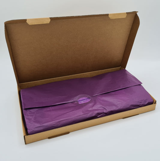 Open brown letterbox friendly cardboard box with the contents folded into purple tissue paper and sealed with a sticker showing the logo for Momento. 