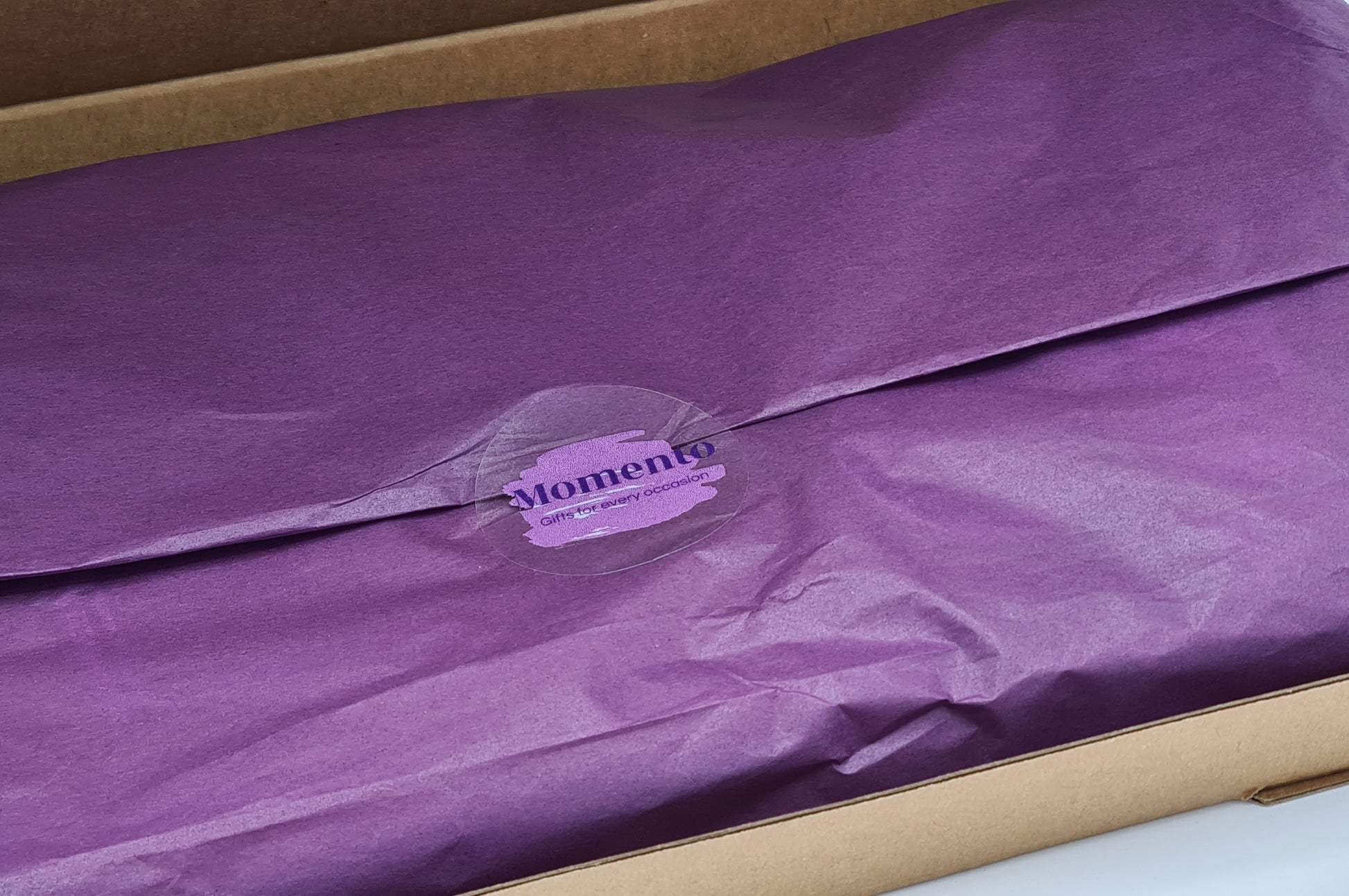 Close up of inside of box with contents wrapped in purple tissue paper which is sealed with a sticker showing the Momento logo.