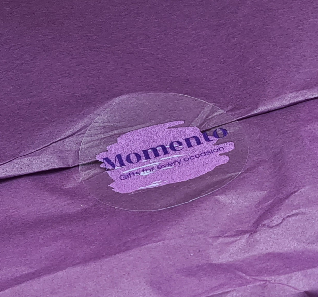 Close up of sticker bearing the Momento Gifts logo and sealing purple tissue.