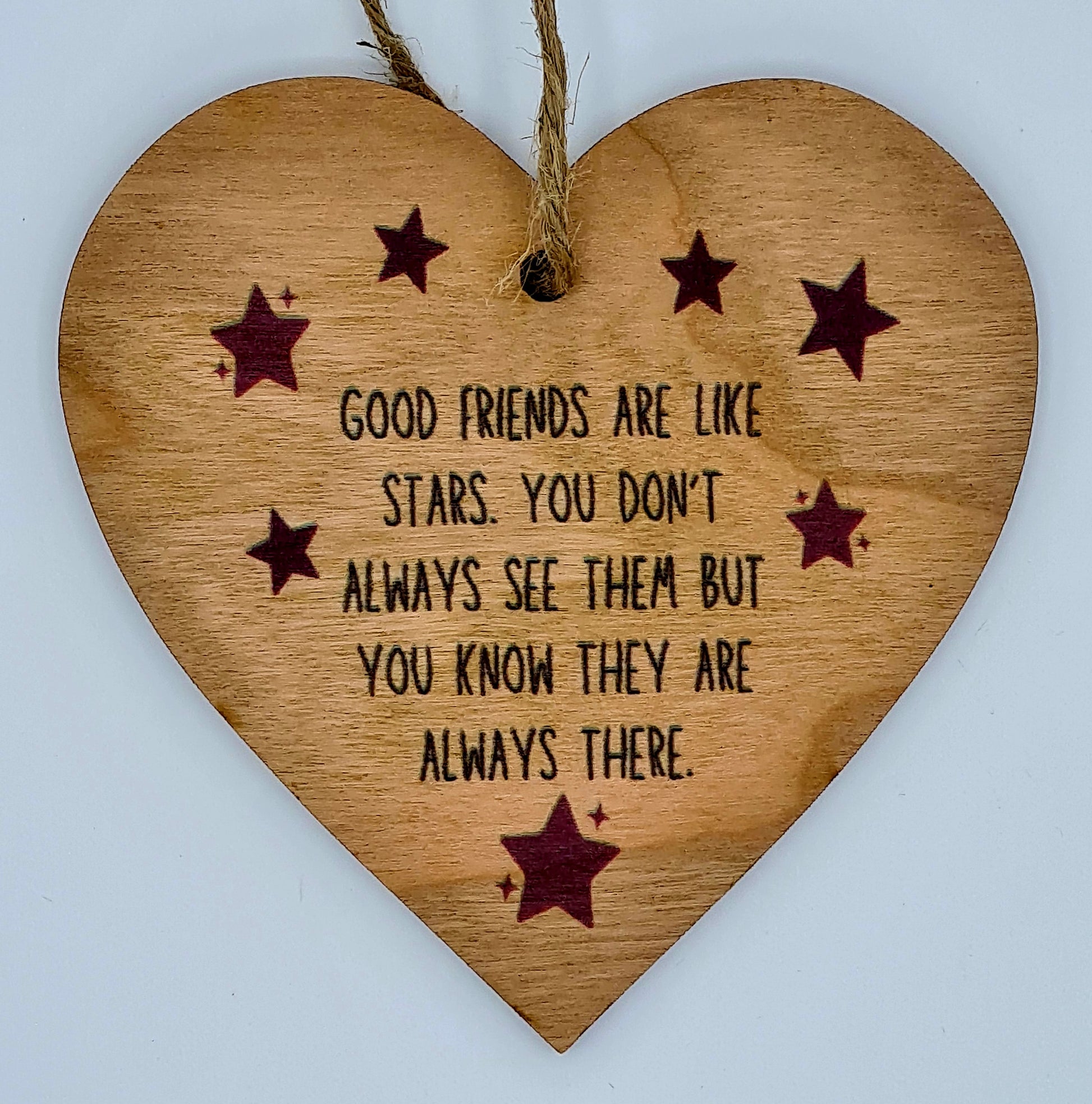 Heart shaped wooden plaque with the slogan "Good friends are like stars. You don't always see them but you know they are always there". There are little red stars around the writing and there is a jute string at the top of the plaque for hanging.