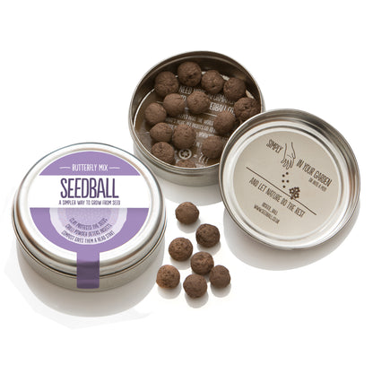 Two silver tins from Seedball. The first tin is closed and has a lilac label with "Butterfly Mix" while the other tin is open - in the bottom half of the tin there are 14 visible seedballs whilst the top half of the tin has an inner label stating "Simply scatter (illustrated by a drawing of a hand scattering the seeds) in your garden or into a pot and let nature do the rest". There are 6 seedballs placed between the two tins.